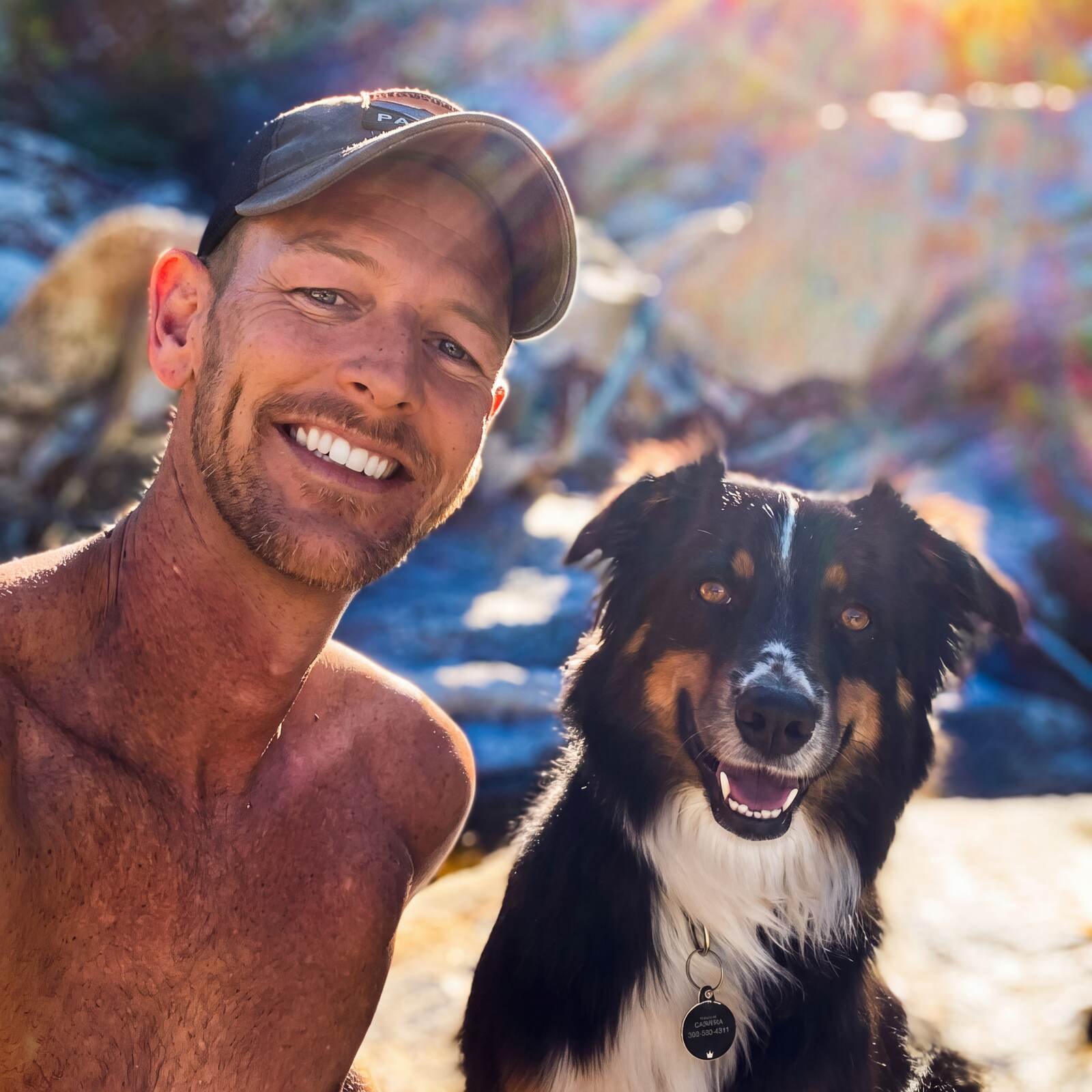 Kira, an Australian Shepherd, posing for a sunny selfie with her other dad, both smiling outdoors
